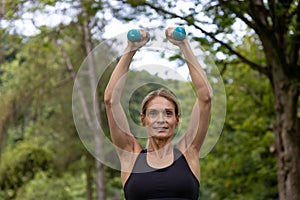 Sporty woman exercising with dumbbells outdoors has physical activity in park.