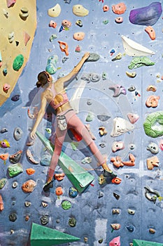 Sporty woman with fit body climbs up the wall in a bouldering gym. Back view rock climber girl workout