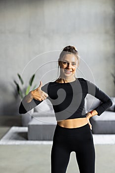 Sporty woman holding balled up exercise mat giving thumb up in bright room