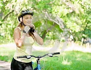 Sporty woman on mountain bike putting biking helmet