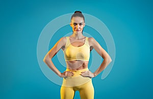 Sporty Woman Posing Wearing Yellow Fitwear Standing On Blue Background