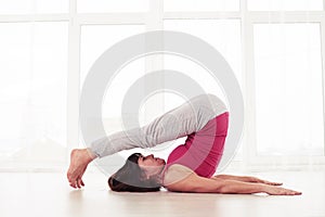 Sporty woman practicing halasana plow pose on the mat in the gym