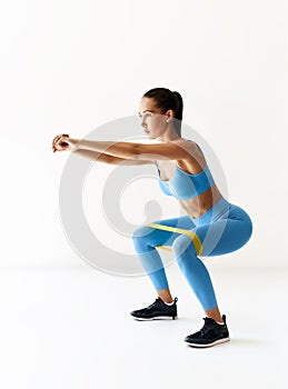 Sporty woman practicing squat exercises with resistance band loop over white background