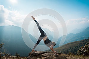 Sporty woman practicing yoga on mountain cliff at sunrise. Healthy lifestyle.