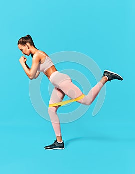 Sporty woman with resistance band loop workouts on blue background