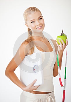 Sporty woman with scale, apple and measuring tape