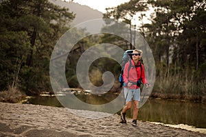 Sporty woman in sportwear walking near the pond with hiking backpack