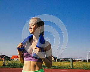 A sporty woman stands at the stadium. A girl wipes her face with a towel after training. Sportswear