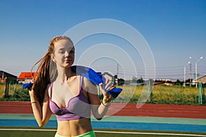 A sporty woman stands at the stadium. A girl wipes her face with a towel after training. Sportswear