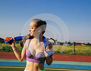 A sporty woman stands at the stadium. A girl wipes her face with a towel after training. Sportswear