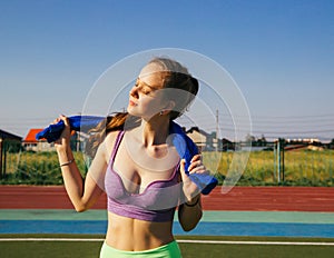 A sporty woman stands at the stadium. A girl wipes her face with a towel after training. Sportswear