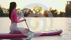 Sporty woman swimming on paddle board on city lake