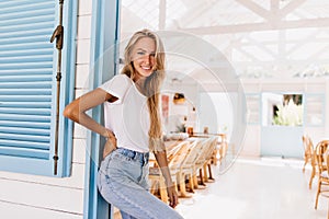 Sporty woman in trendy denim pants standing in cafeteria. Indoor shot of magnificent caucasian girl