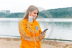 Sporty woman is walking and using her earpods and phone near a forest lake.