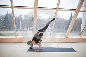 Sporty woman working out, doing arm balancing handstand yoga asana, One Legged Crane Pose, Half Crow Pose, eka pada galavasana of