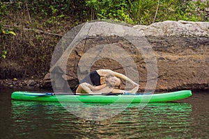 Sporty woman in yoga position on paddleboard, doing yoga on sup board, exercise for flexibility and stretching of