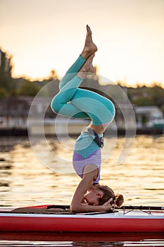 Sporty woman in yoga position on paddleboard, doing yoga on sup board, exercise for flexibility and stretching of