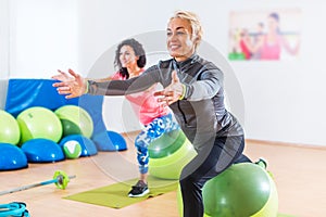 Sporty women doing stretching exercises with fitness stability ball in a sports club