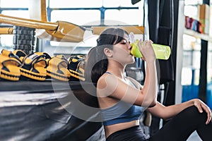 Sporty young asian woman after successful workout in fitness gym holding bottle of protein shake