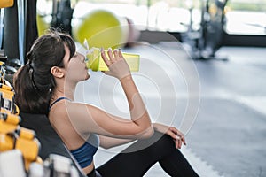 Sporty young asian woman after successful workout in fitness gym holding bottle of protein shake