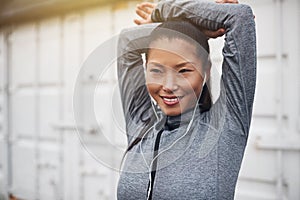 Sporty young Asian woman wearing earphones stretching before jog