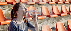 Sporty young attractive girl in sportswear relaxing after hard workout sit and drink water from special sport bottle after running