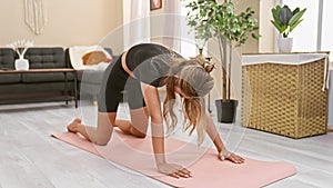 Sporty young blonde woman engaging in a serious abdominal stretching exercise at home, focusing on concentration as she improves