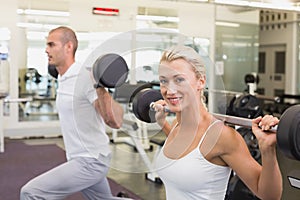 Sporty young couple lifting barbells in gym