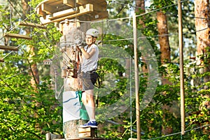 Sporty, young, cute boy in white t shirt spends his time in adventure rope park in helmet and safe equipment in the park