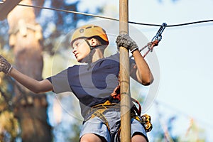 Sporty, young, cute boy in white t shirt spends his time in adventure rope park in helmet and safe equipment in the park