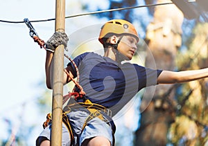 Sporty, young, cute boy in white t shirt spends his time in adventure rope park in helmet and safe equipment in the park