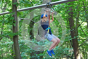 Sporty, young, cute boy in white t shirt spends his time in adventure rope park in helmet and safe equipment in the park