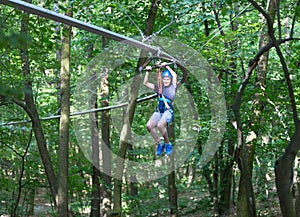 Sporty, young, cute boy in white t shirt spends his time in adventure rope park in helmet and safe equipment in the park