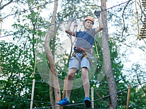 Sporty, young, cute boy in white t shirt spends his time in adventure rope park in helmet and safe equipment in the park