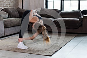 Sporty young female doing stretching exercise bending forward during home workout