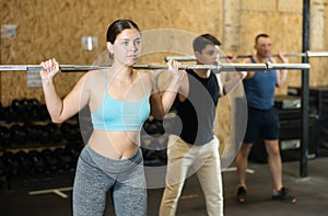 Sporty young girl doing exercises with barbell in gym