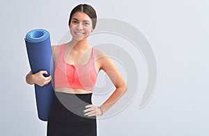 Sporty young girl holding yoga mat doing asana over bright gray background