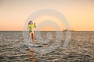 Sporty young girl stand up paddle surfing with beautiful sunset colors