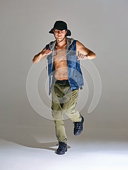 Sporty young man breakdancer in hat dancing hip-hop in studio  on gray background. Break dance lessons
