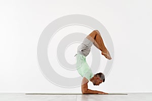 Sporty young man doing backbend handstand, yoga, pilates, fitness training, standing in chin balance asana