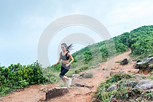 Sporty young woman in black sportswear trail running on mountain nature path. Fit girl jogging downhill rocky track.