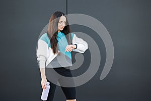 Sporty young woman checks results of fitness training and holds bottle with fresh water, dressed in activewear poses outdoors.