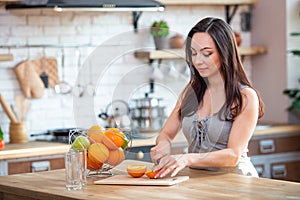 Sporty young woman is cutting fresh orange for fruit juice in the kitchen. Horizontal indoors shot