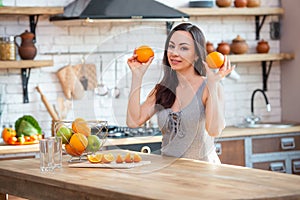 Sporty young woman is cutting fresh orange for fruit juice in the kitchen. Horizontal indoors shot