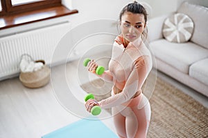 Sporty young woman exercising at home with dumbbells