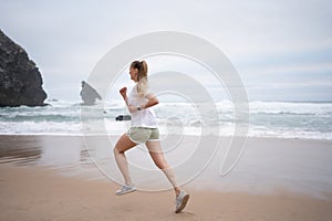 Sporty young woman jogging on sandy beach along sea