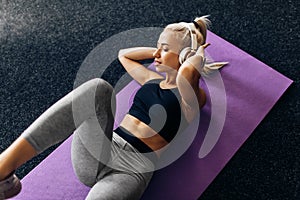 Sporty young woman listening to music with headphones doing ab exercises on fitness mat in gym