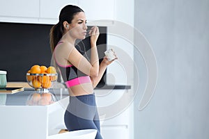 Sporty young woman listening to music with mobile phone while eating yogurt in the kitchen at home