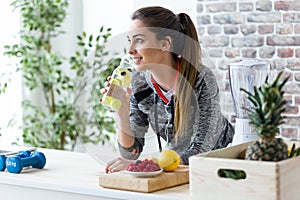 Sporty young woman looking sideways while drinking lemon juice in the kitchen at home.