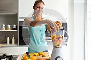 Sporty young woman making a vegetable smoothie while listening to music in her kitchen.